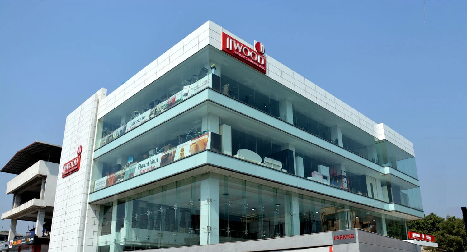 The JJ Wood showroom in Panvel — a multi-storey glass-fronted building with the JJ Wood sign and street-level parking